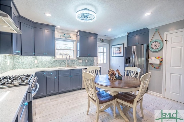 kitchen with a sink, wall chimney range hood, appliances with stainless steel finishes, crown molding, and light countertops