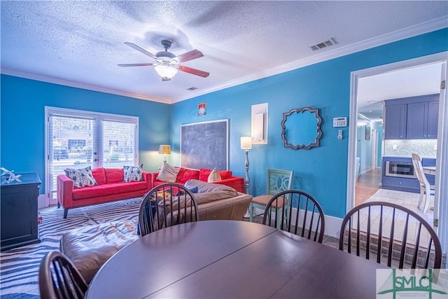 dining area with ceiling fan, a textured ceiling, visible vents, and ornamental molding