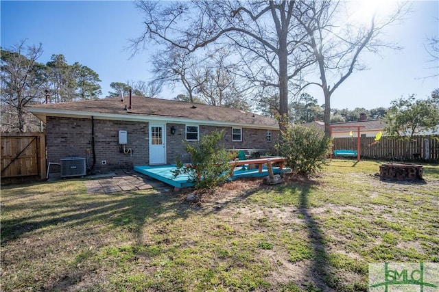 back of property with a yard, central air condition unit, brick siding, and fence