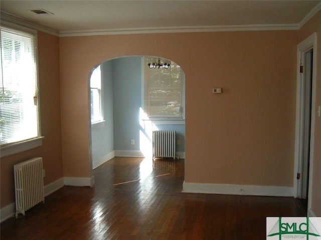 unfurnished room featuring radiator heating unit, wood finished floors, arched walkways, and ornamental molding