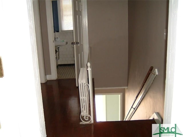 corridor with wood finished floors, radiator heating unit, and an upstairs landing