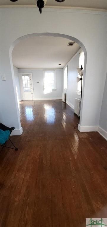 unfurnished living room featuring visible vents, arched walkways, dark wood-style flooring, and baseboards