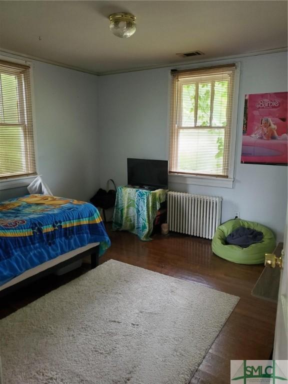 bedroom featuring visible vents, wood finished floors, radiator heating unit, and crown molding