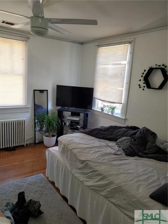 bedroom featuring multiple windows, radiator heating unit, wood finished floors, and ceiling fan