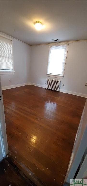 empty room featuring visible vents, radiator heating unit, baseboards, and wood finished floors