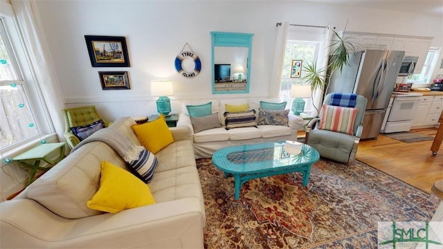 living area with a wainscoted wall, a healthy amount of sunlight, and light wood-type flooring