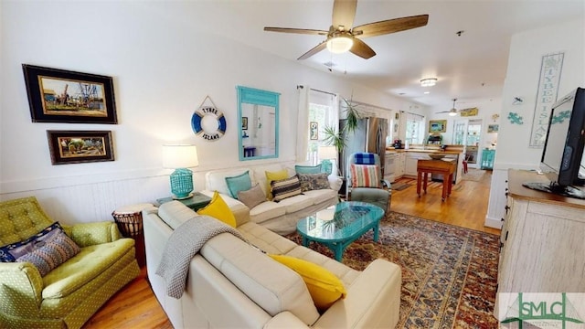 living room with a ceiling fan, light wood finished floors, and wainscoting