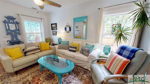 living area featuring visible vents, a ceiling fan, and a wainscoted wall