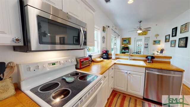 kitchen with a peninsula, white cabinets, appliances with stainless steel finishes, and a sink