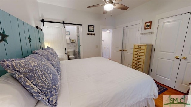 bedroom with two closets, a ceiling fan, wood finished floors, connected bathroom, and a barn door