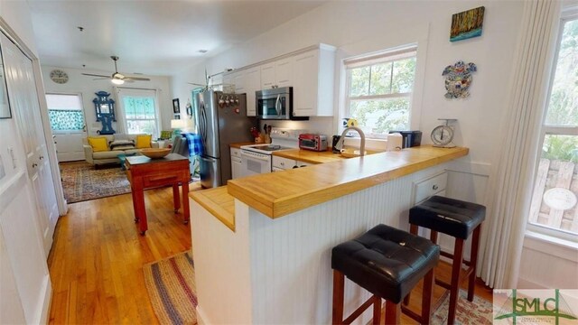 kitchen featuring a breakfast bar area, a wealth of natural light, light wood-style flooring, stainless steel appliances, and white cabinetry