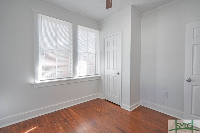 empty room featuring a textured ceiling, crown molding, baseboards, ceiling fan, and dark wood-style flooring