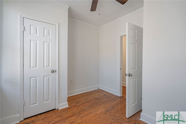 empty room with ornamental molding, a ceiling fan, a textured ceiling, wood finished floors, and baseboards