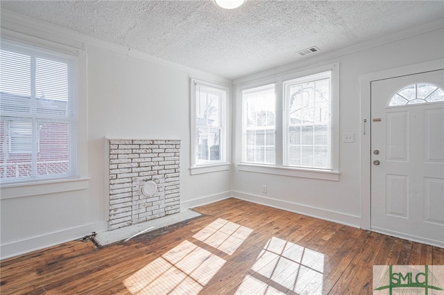 entrance foyer with hardwood / wood-style floors, baseboards, visible vents, ornamental molding, and a textured ceiling