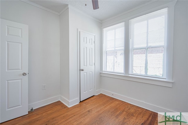 unfurnished bedroom with light wood-type flooring, ornamental molding, a ceiling fan, a textured ceiling, and baseboards