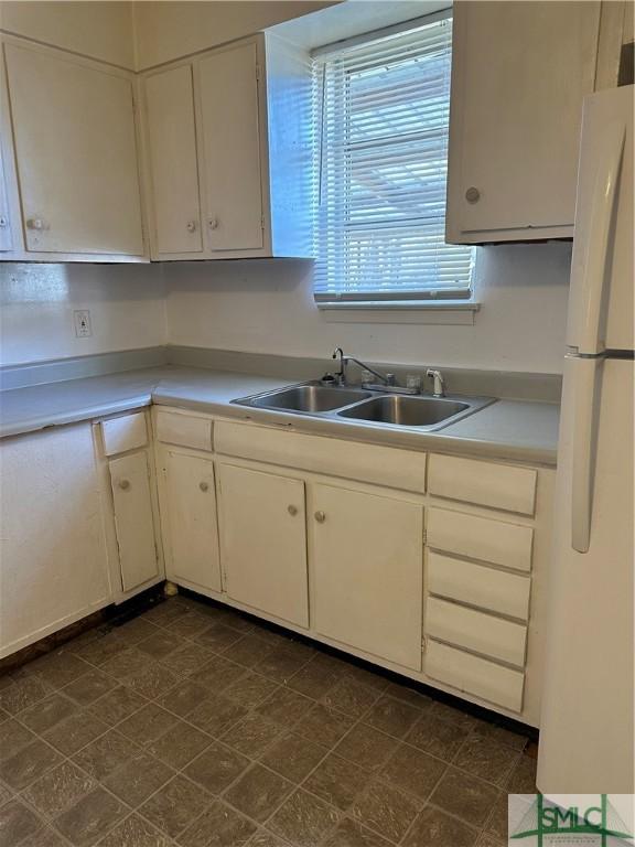 kitchen with white cabinetry, light countertops, freestanding refrigerator, and a sink