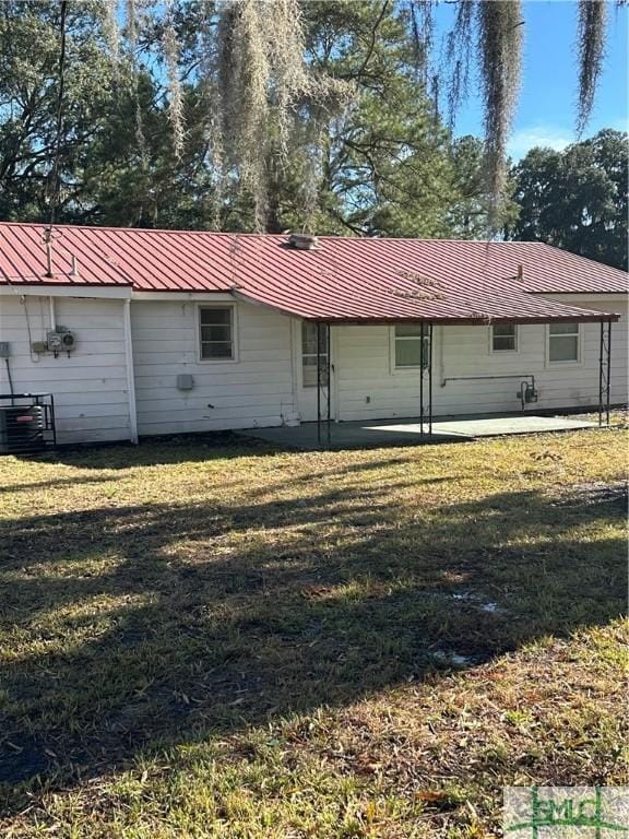 rear view of house with metal roof, a patio, and a lawn