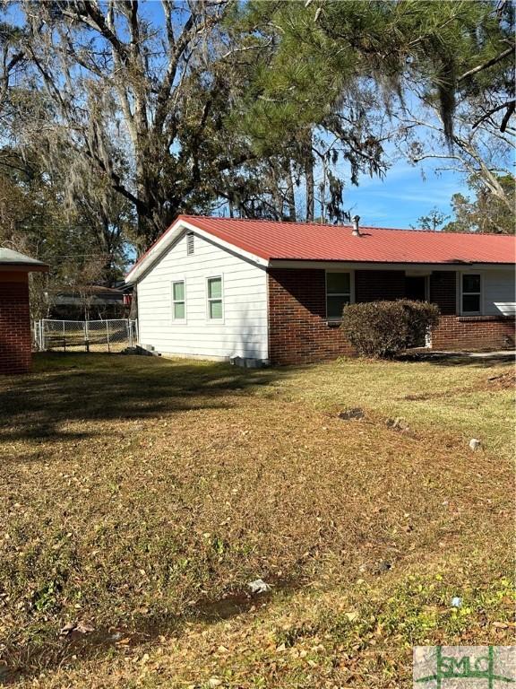 view of side of property with brick siding, a lawn, and fence