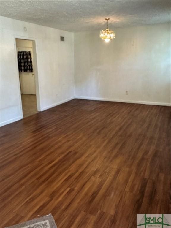 spare room featuring a chandelier, a textured ceiling, baseboards, and wood finished floors