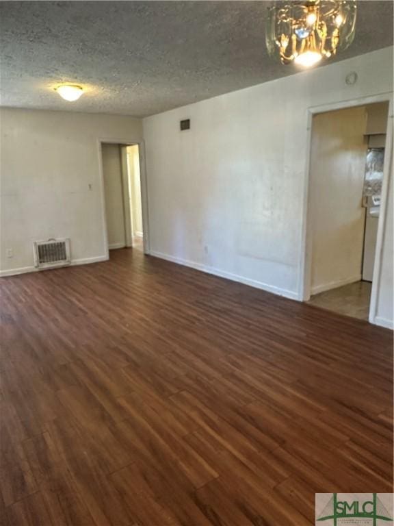 spare room featuring visible vents, dark wood-type flooring, a textured ceiling, an inviting chandelier, and baseboards