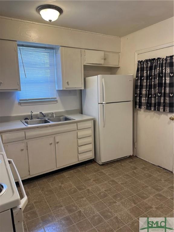 kitchen with freestanding refrigerator, a sink, light countertops, white cabinetry, and dark floors