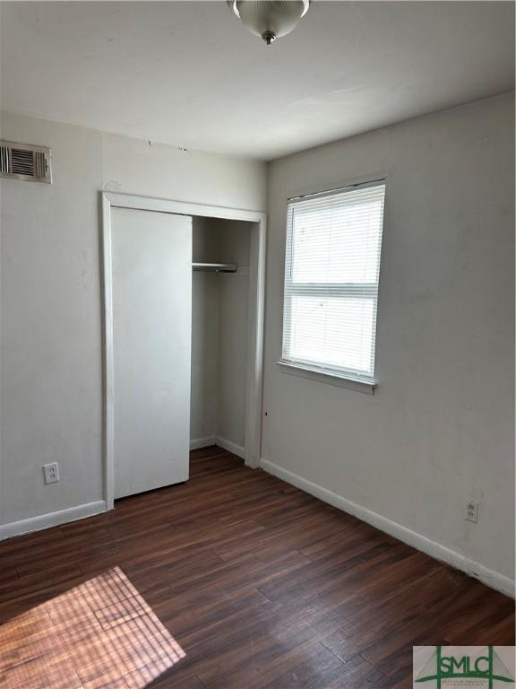 unfurnished bedroom featuring wood finished floors, visible vents, a closet, and baseboards