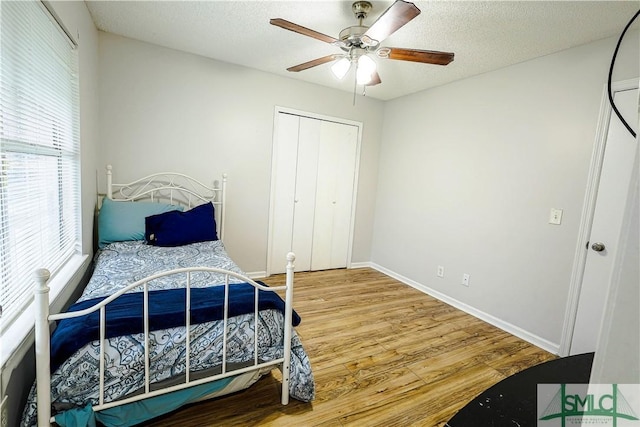 bedroom featuring baseboards, wood finished floors, a closet, a textured ceiling, and a ceiling fan