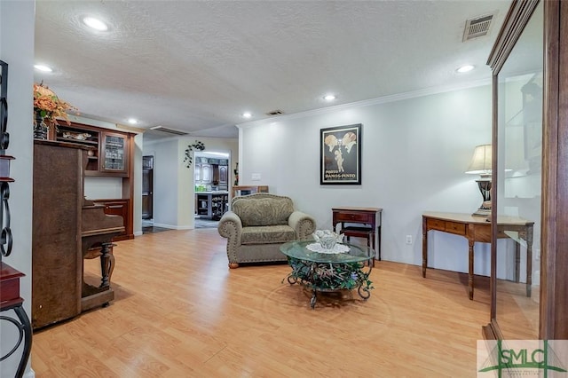 living area featuring visible vents, a textured ceiling, crown molding, and light wood-style floors