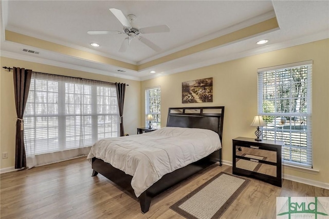 bedroom featuring visible vents, a raised ceiling, multiple windows, and wood finished floors