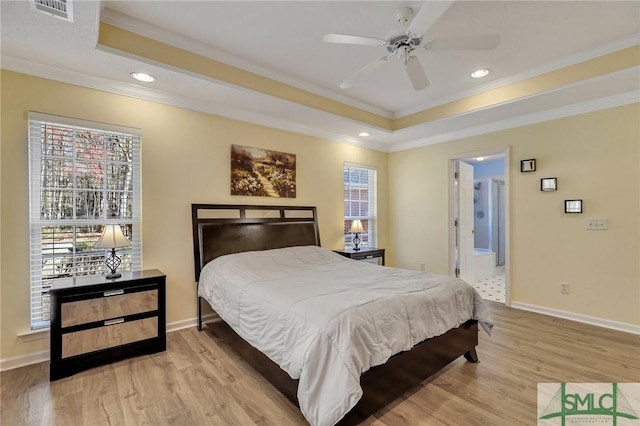 bedroom with a tray ceiling, visible vents, ornamental molding, and light wood finished floors