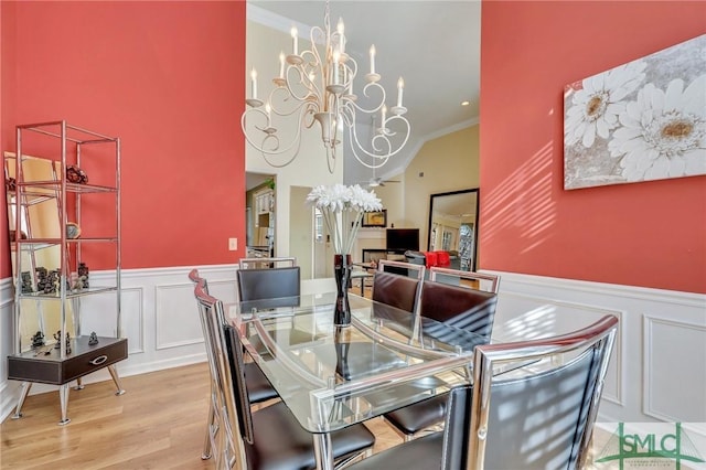 dining area featuring an inviting chandelier, wood finished floors, crown molding, and wainscoting