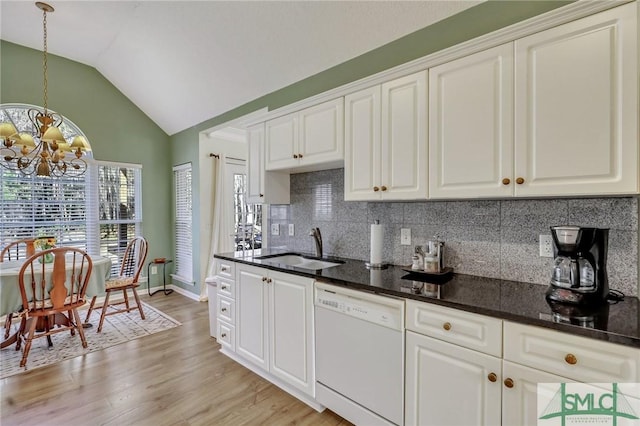 kitchen featuring lofted ceiling, white dishwasher, a sink, decorative backsplash, and a chandelier