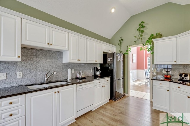 kitchen featuring lofted ceiling, white dishwasher, freestanding refrigerator, a sink, and white cabinets