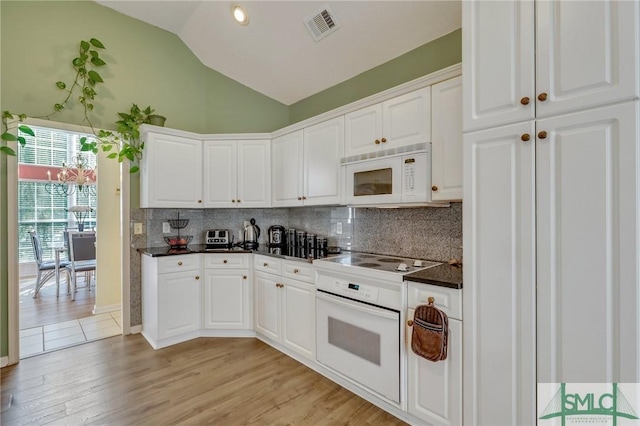 kitchen with dark countertops, visible vents, vaulted ceiling, white appliances, and white cabinetry