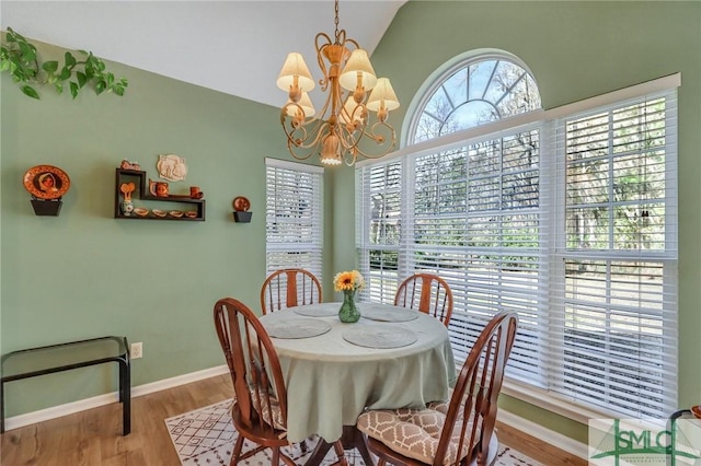 dining area featuring lofted ceiling, a notable chandelier, wood finished floors, and baseboards