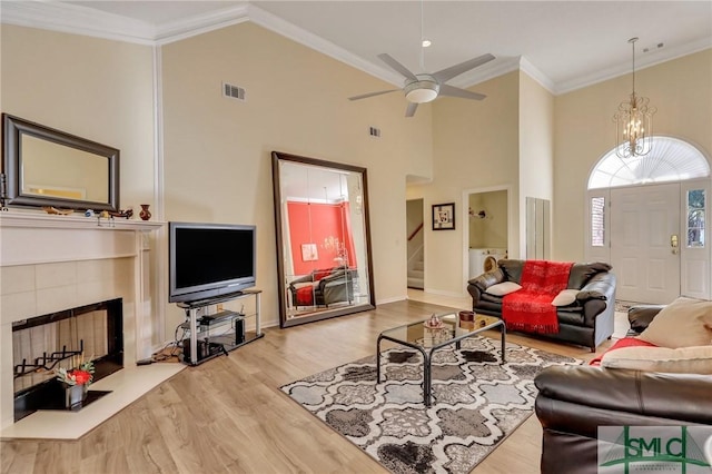 living room with visible vents, crown molding, a tiled fireplace, stairway, and wood finished floors