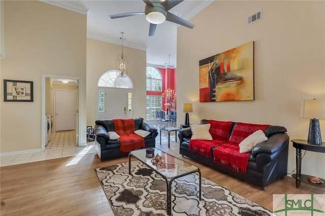 living area featuring wood finished floors, visible vents, baseboards, a towering ceiling, and crown molding