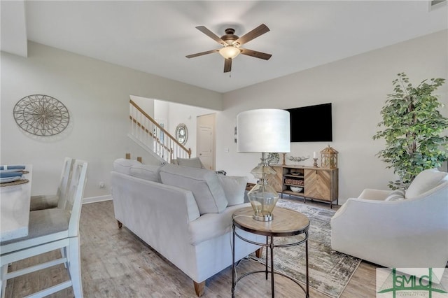 living area featuring baseboards, stairs, a ceiling fan, and wood finished floors