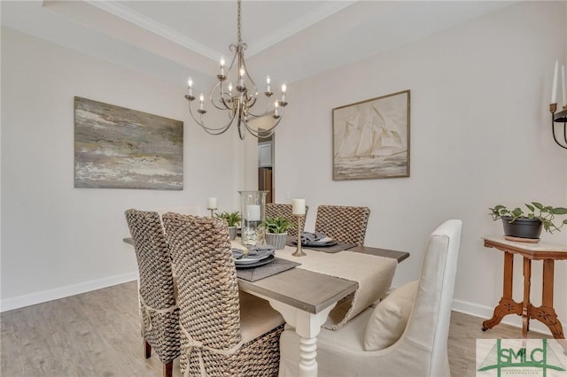 dining room featuring baseboards, a raised ceiling, light wood-style flooring, and crown molding