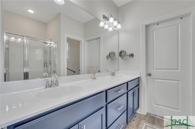 full bathroom with double vanity, a shower stall, wood finished floors, and a sink