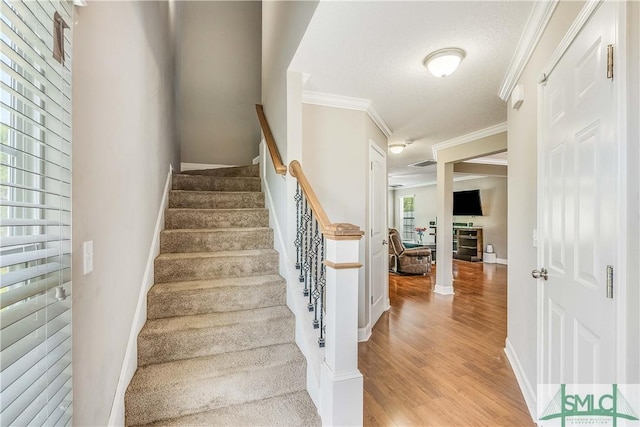 stairway featuring crown molding, wood finished floors, baseboards, and a textured ceiling