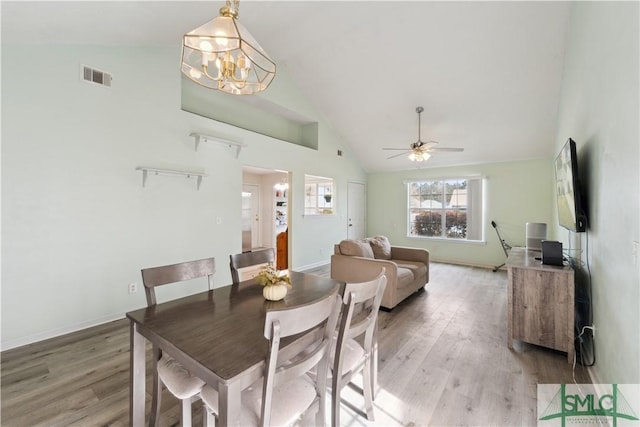 dining room with visible vents, ceiling fan with notable chandelier, high vaulted ceiling, and light wood finished floors