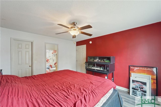 bedroom featuring a ceiling fan, wood finished floors, baseboards, ensuite bath, and a textured ceiling