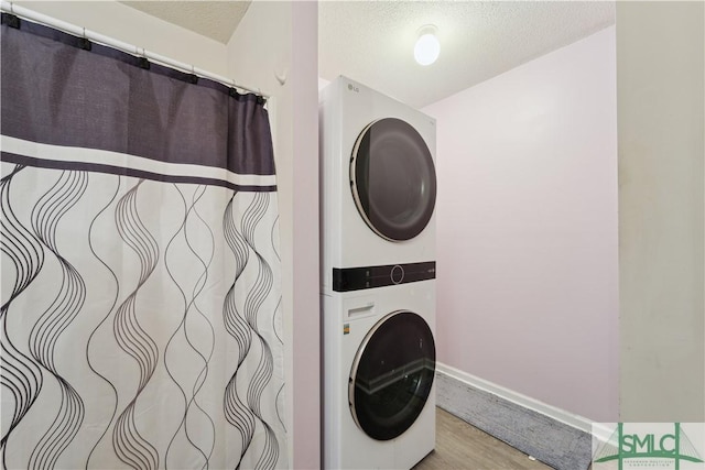 clothes washing area with stacked washer / dryer, a textured ceiling, laundry area, and wood finished floors