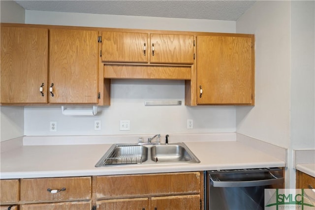 kitchen with light countertops, stainless steel dishwasher, brown cabinetry, a textured ceiling, and a sink