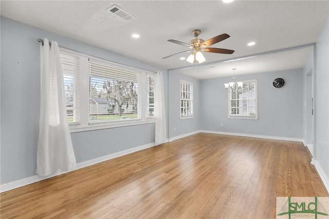 empty room featuring visible vents, baseboards, ceiling fan with notable chandelier, and light wood finished floors