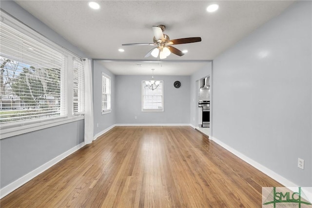 unfurnished living room featuring recessed lighting, light wood-style flooring, ceiling fan with notable chandelier, and baseboards