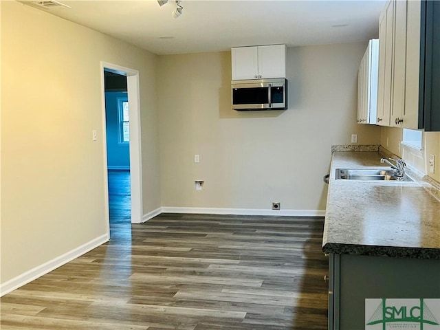 kitchen with wood finished floors, baseboards, a sink, white cabinetry, and stainless steel microwave