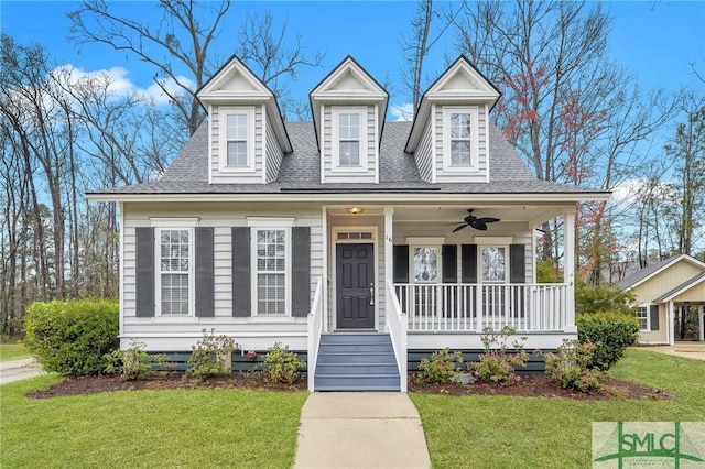 new england style home featuring roof with shingles, covered porch, ceiling fan, and a front yard