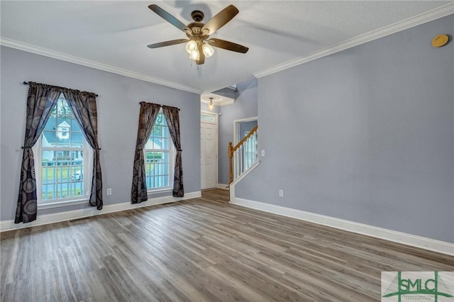 empty room featuring crown molding, baseboards, stairs, wood finished floors, and a ceiling fan